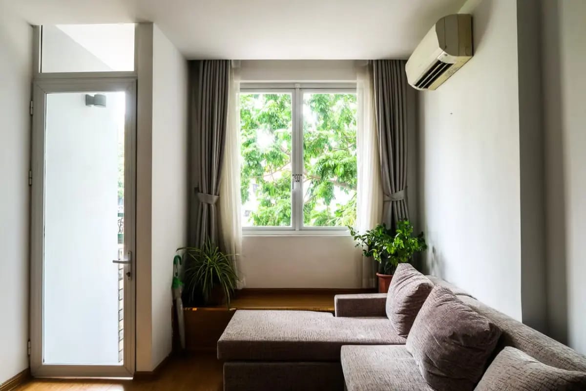 Wall-mounted AC unit in a home with sofa and plants.